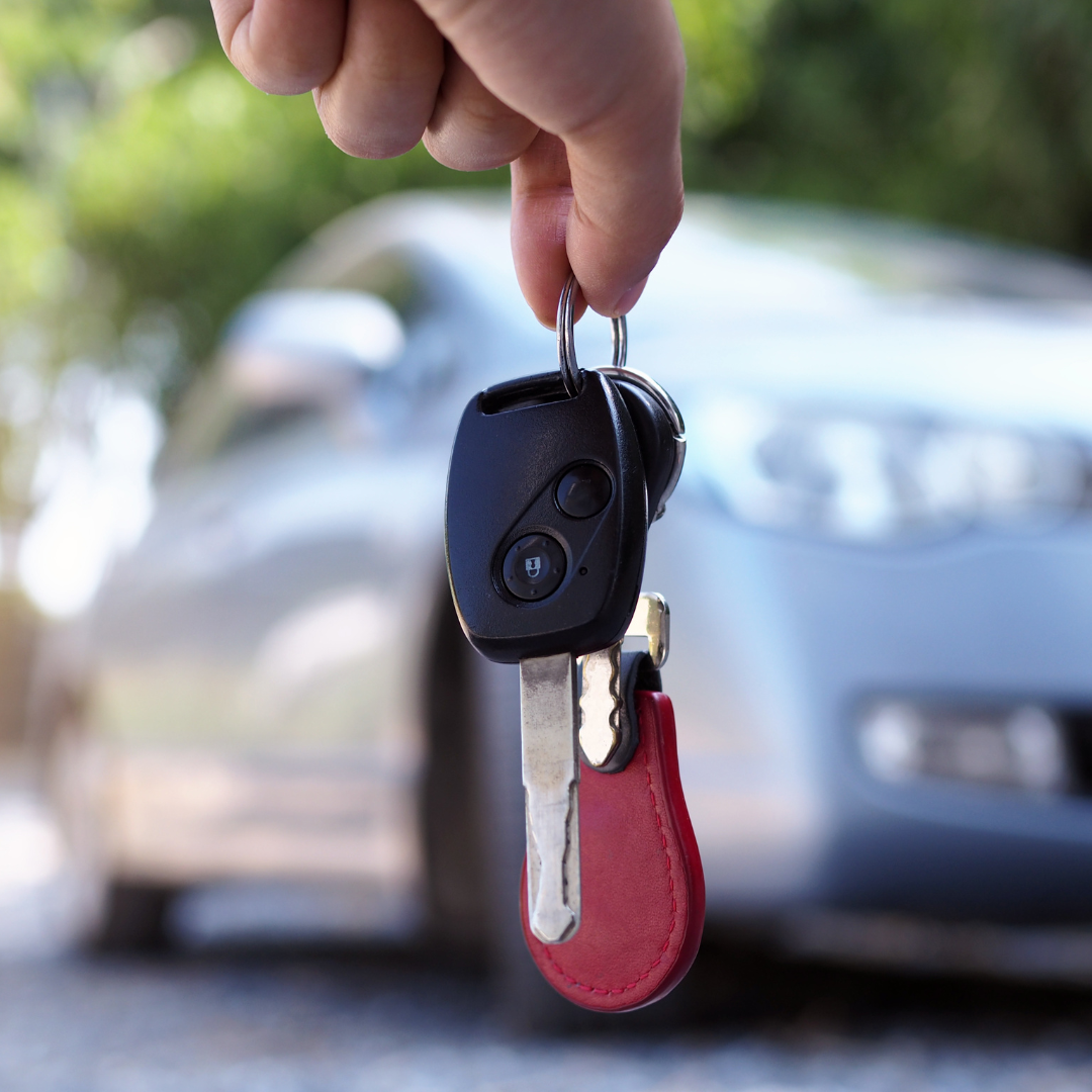 imagem de uma pessoa segurando uma chave de um carro desfocado ao fundo.